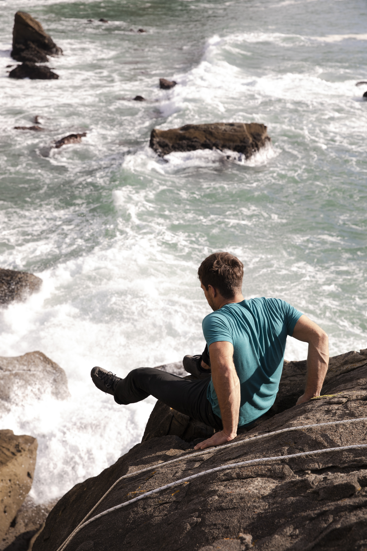Photograph of a man perched on a boulder over the Sonoma Coast in California as pro climbing Kevin Jorgeson prepares to make a first ascent of a highball boulder problem.
