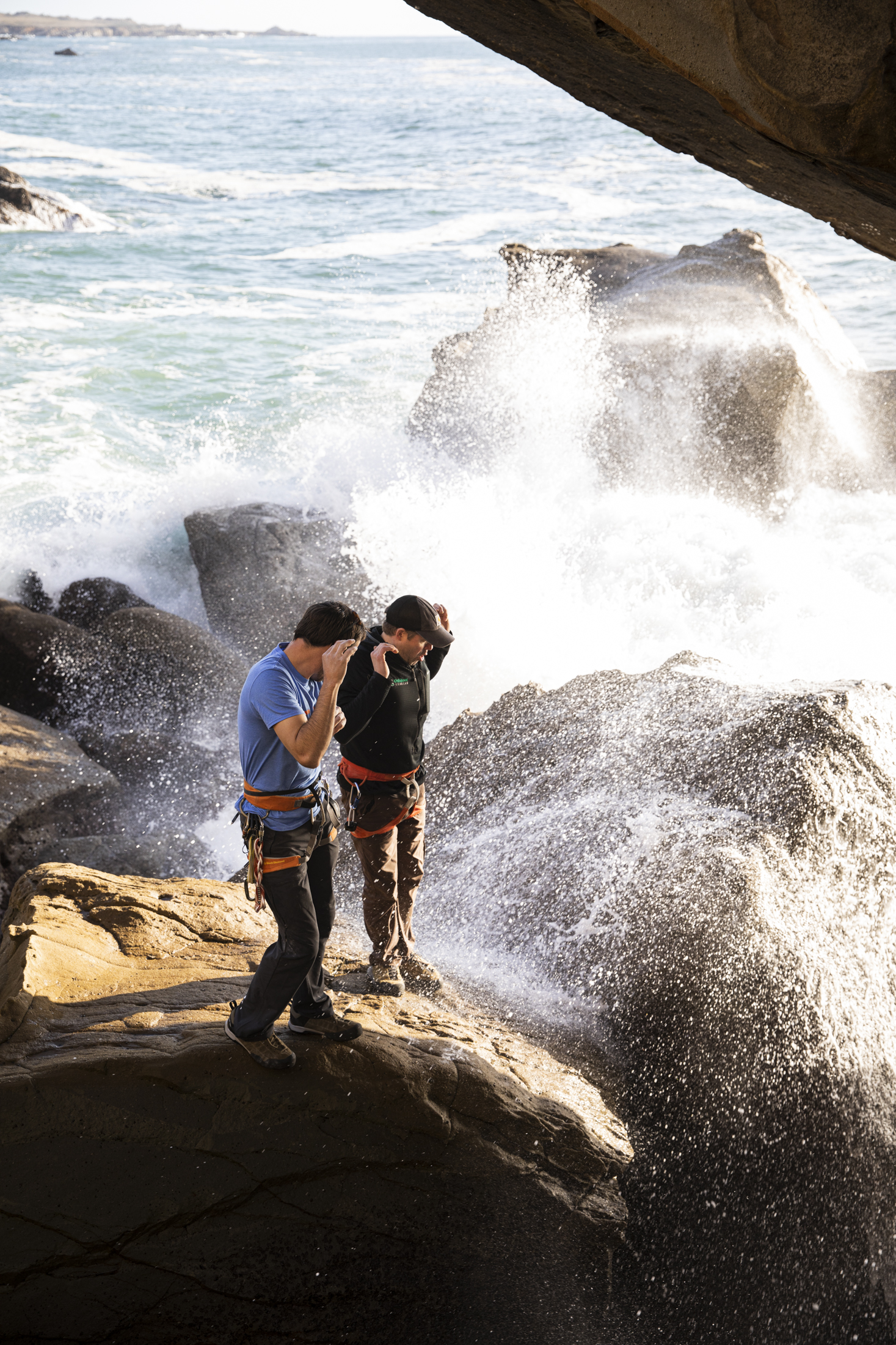 Photograph of climbers Kevin Jorgeson and Chris Summit getting splashed by a sneaker wave at the base of the then under-development boulder problem on California's Sonoma Coast.